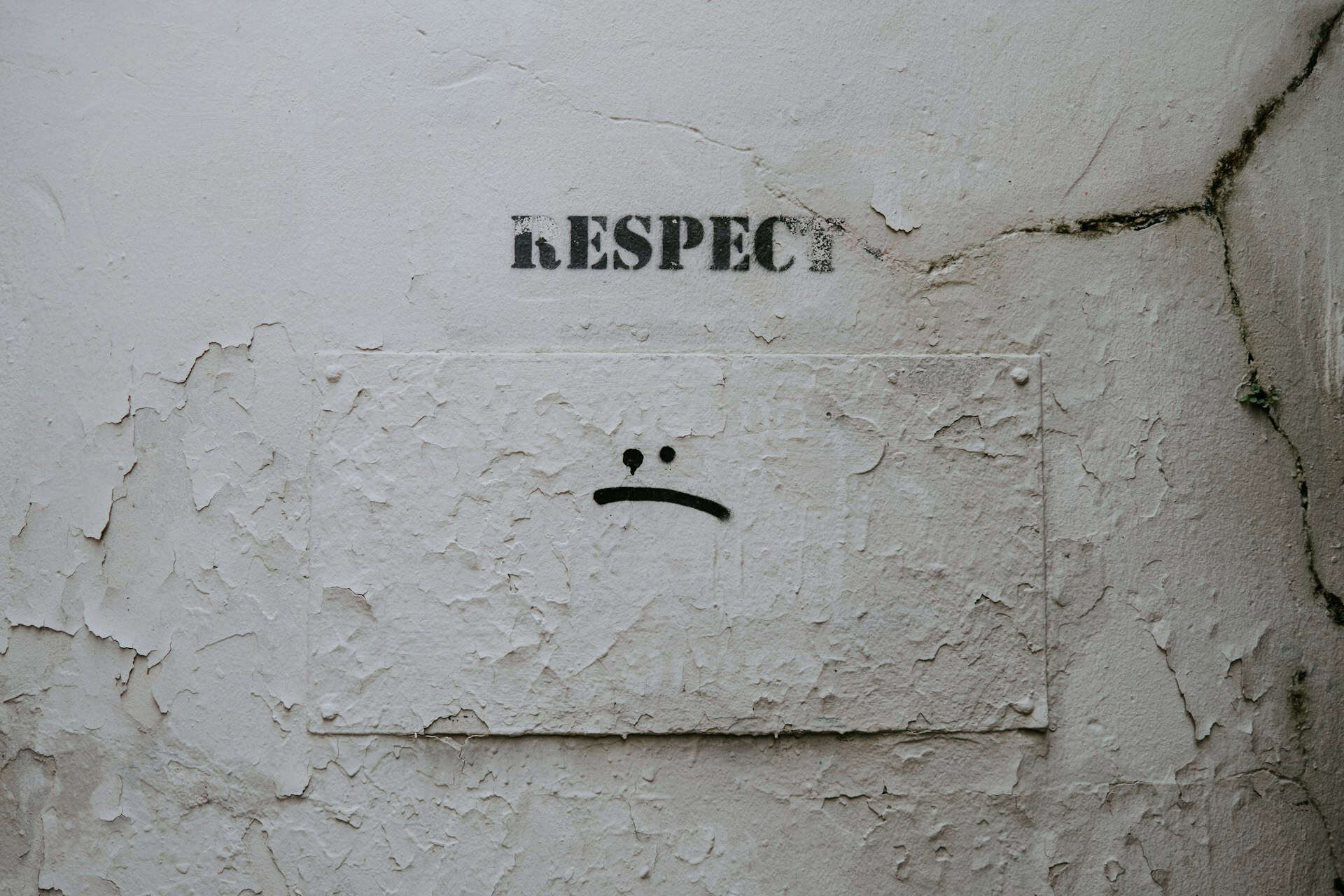 A stencil saying "Respect" and a painted sad face, both on a wall.